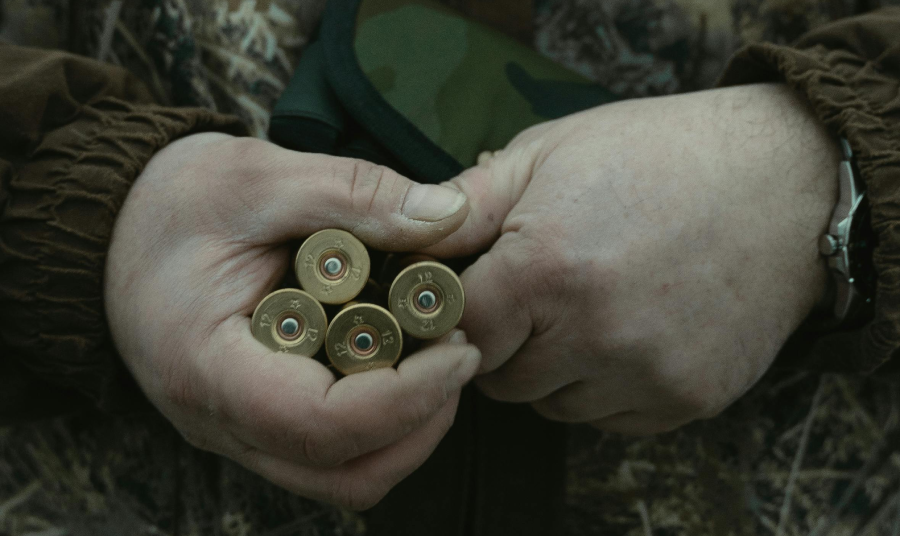 a close-up of hands holding several cartridges, with the focus on the brass casing and the primer of each round.