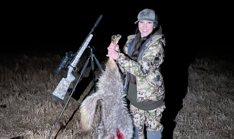 a female hunter posing proudly with her catch, which appears to be a coyote.